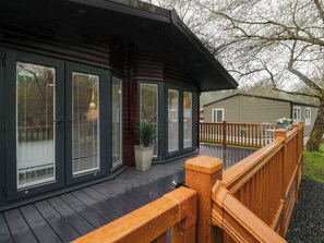 A wooden deck with a railing, a potted plant, and a building with large windows and a door. - Robin's Lodge (Windermere)