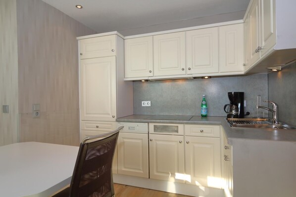 A compact kitchen with white cabinets, a stainless steel sink, and a coffee maker. - House Captain Christiansen 46 (Westerland)