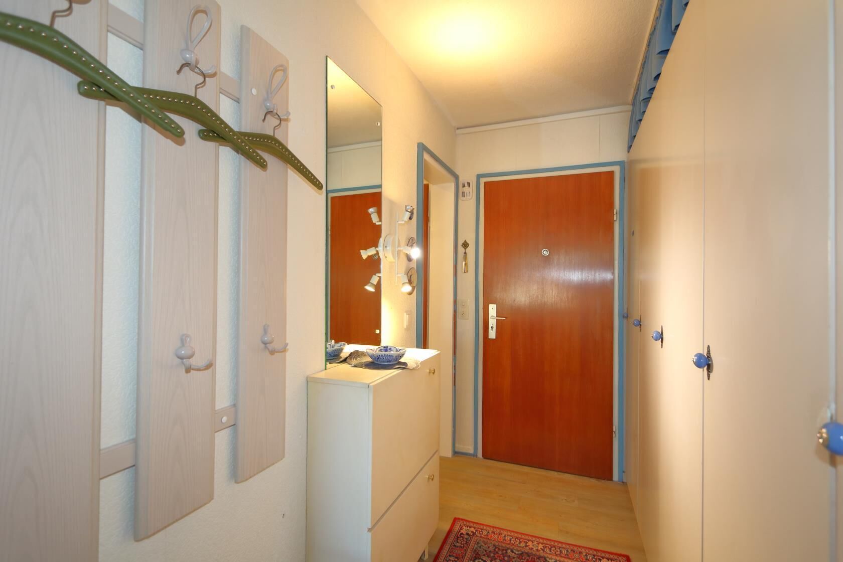A hallway with a wooden door, a mirror, a small sink, and a patterned rug.