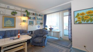 A living room with a sofa, armchair, table, and bookshelf. - House Captain Christiansen 53 (Westerland)