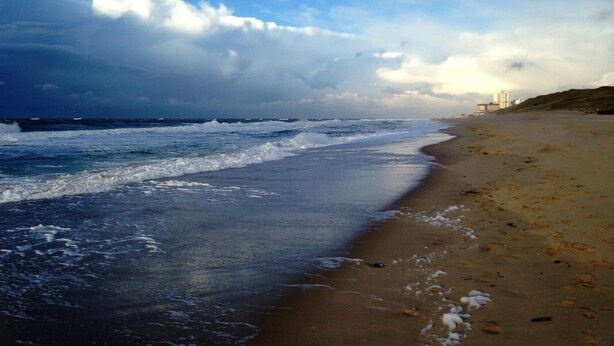 A beach with waves, a clear sky, and a distant building. - House Captain Christiansen 53 (Westerland)