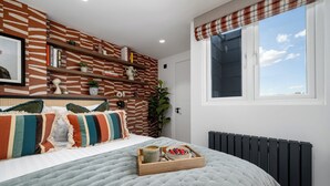 Une chambre à coucher comprenant un lit, une fenêtre, un radiateur et une étagère avec des livres et des objets décoratifs.