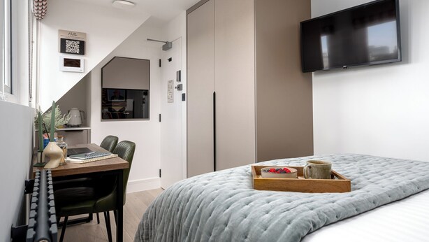 Une chambre moderne avec un lit, un bureau avec un ordinateur portable, un téléviseur fixé au mur et une armoire.