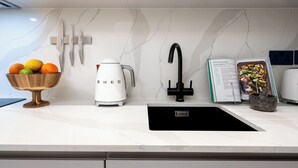 A modern kitchen with a white marble backsplash, a black faucet, a white coffee maker, and a bowl of fruit. - Camden | Studio W Separate Kitchen (London)