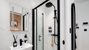 A modern bathroom with a white marble sink, a glass shower enclosure, and a black showerhead. - Camden | Studio W Separate Kitchen (London)