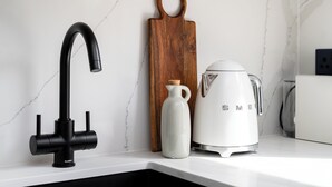 A kitchen with a modern faucet, a wooden cutting board, a white pitcher, and a white coffee maker. - Camden | Studio - Studio Apartment, Sleeps 2 (London)