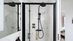 A modern bathroom with a glass-enclosed shower, marble walls, and a visible sink area with toiletries. - Camden | Studio - Studio Apartment, Sleeps 2 (London)