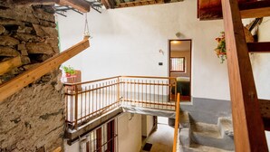Interior rústico com parede de pedra, vigas de madeira, escada de madeira e uma pequena mesa com um vaso de planta.