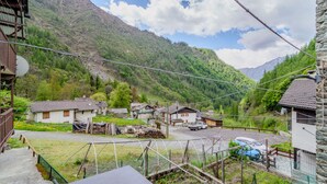 Uma aldeia rural com casas tradicionais, estrada de cascalho e montanhas ao fundo.