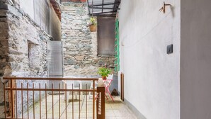 Um pátio estreito com paredes de pedra, um portão de madeira e uma pequena mesa com um vaso de planta.