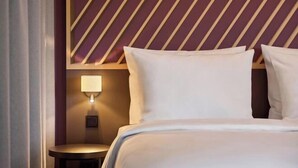 A hotel room with a bed, a nightstand, a wall-mounted lamp, and a patterned wall. - B&B HOTEL München City-Nord (Munich)