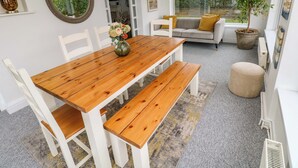 A dining area with a wooden table and white chairs, a sofa with yellow cushions, and a potted plant by the window. - Burry House (Swansea)