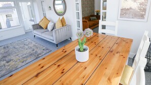 A modern living room with a wooden dining table, a grey sofa with cushions, a round mirror, and a view through an open door to another room. - Burry House (Swansea)