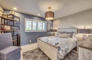 A bedroom with a bed, bedside tables, a chair, a desk, a window, and a ceiling fan.