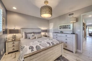A bedroom with a bed, bedside tables, a dresser, and a hanging light fixture.
