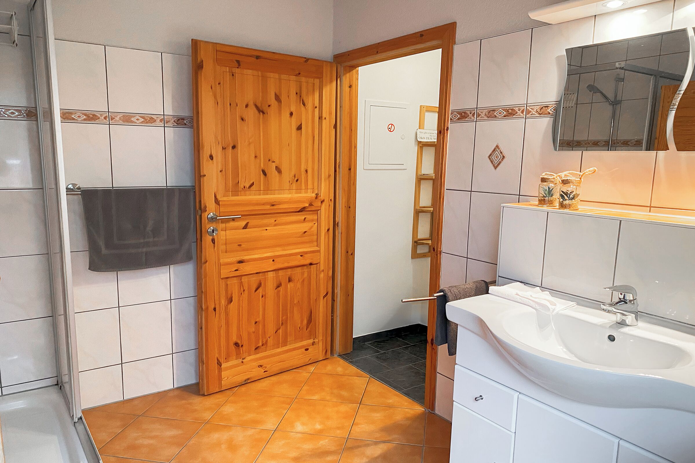 A bathroom with a wooden door, white tiled walls, a white sink, and a mirror above it.