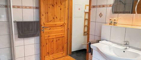 A bathroom with a wooden door, white tiled walls, a white sink, and a mirror above it.