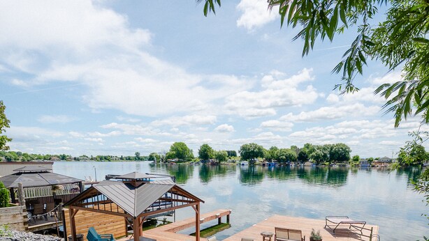 A wooden deck with outdoor furniture, a grill, and a covered seating area overlooking a lake. - Cozy Lakeview Home with Water Access (Cornwall)