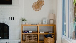 A living room with a fireplace, wooden shelves, wicker baskets, and a large window with curtains. - Cozy Lakeview Home with Water Access (Cornwall)