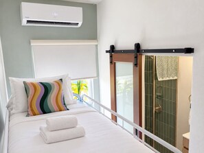 A hotel room with a bed, a window with a view, an air conditioning unit, and a shower area.