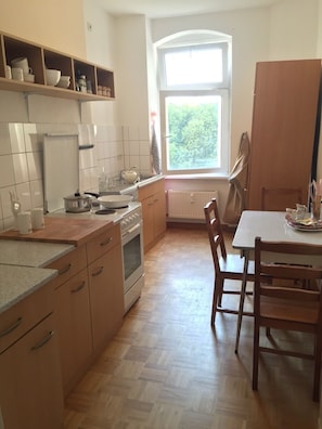 Een keuken met houten kasten, een eettafel, stoelen en een raam met uitzicht op groen.