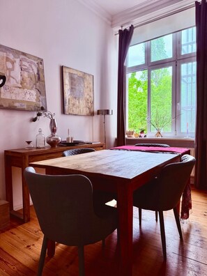 A dining area with a wooden table and chairs, a vase with dried flowers, and artwork on the walls.