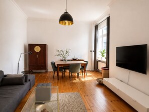 A modern living room with a sofa, a dining table with chairs, a TV, and a wooden cabinet.