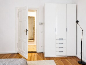 A room with a white wardrobe, a door leading to another room, a floor lamp, and a rug.