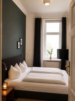 A bedroom with a bed, bedside lamps, a window with curtains, a radiator, and a television.