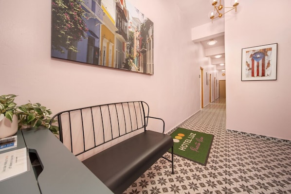 Ein Hotel-Empfangsbereich mit Sitzbank, Rezeption, Blumentopf und Willkommen-Fußmatte.