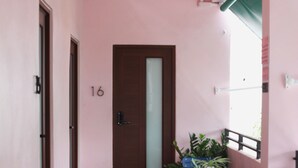 A narrow corridor with a ceiling fan, a door marked with the number 16, and a table with chairs and potted plants.
