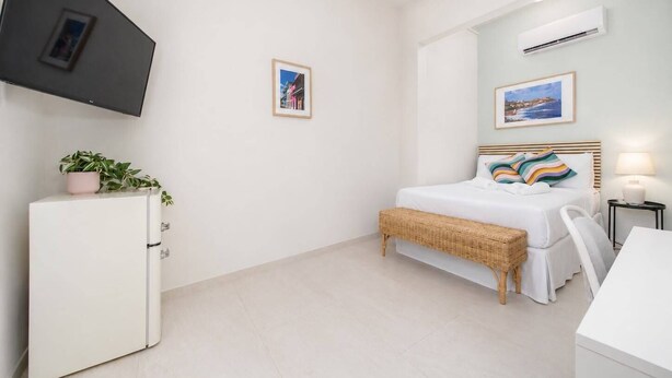 A hotel room with a bed, a TV mounted on the wall, a small table, and a white cabinet. - Skyline Sips and Santurce Charm (San Juan)
