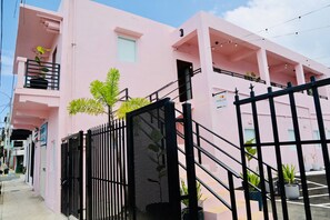 Un bâtiment rose avec une entrée fermée par un portail, une enseigne bien visible indiquant « HÔTEL LUZ », et un escalier menant à l’entrée.