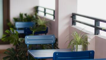 A seating area with blue chairs and tables, potted plants, and a balcony railing.