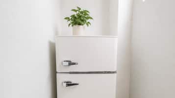 Un réfrigérateur blanc à deux portes, avec une plante en pot posée sur le dessus, et une chaise au premier plan.