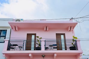 A pink building with a balcony, two windows, and a small table with chairs. - Balcony Bliss in Creative Santurce (San Juan)