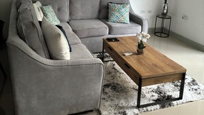 Een moderne woonkamer met een grijze modulaire bank, een houten salontafel en een groot abstract schilderij aan de wand.