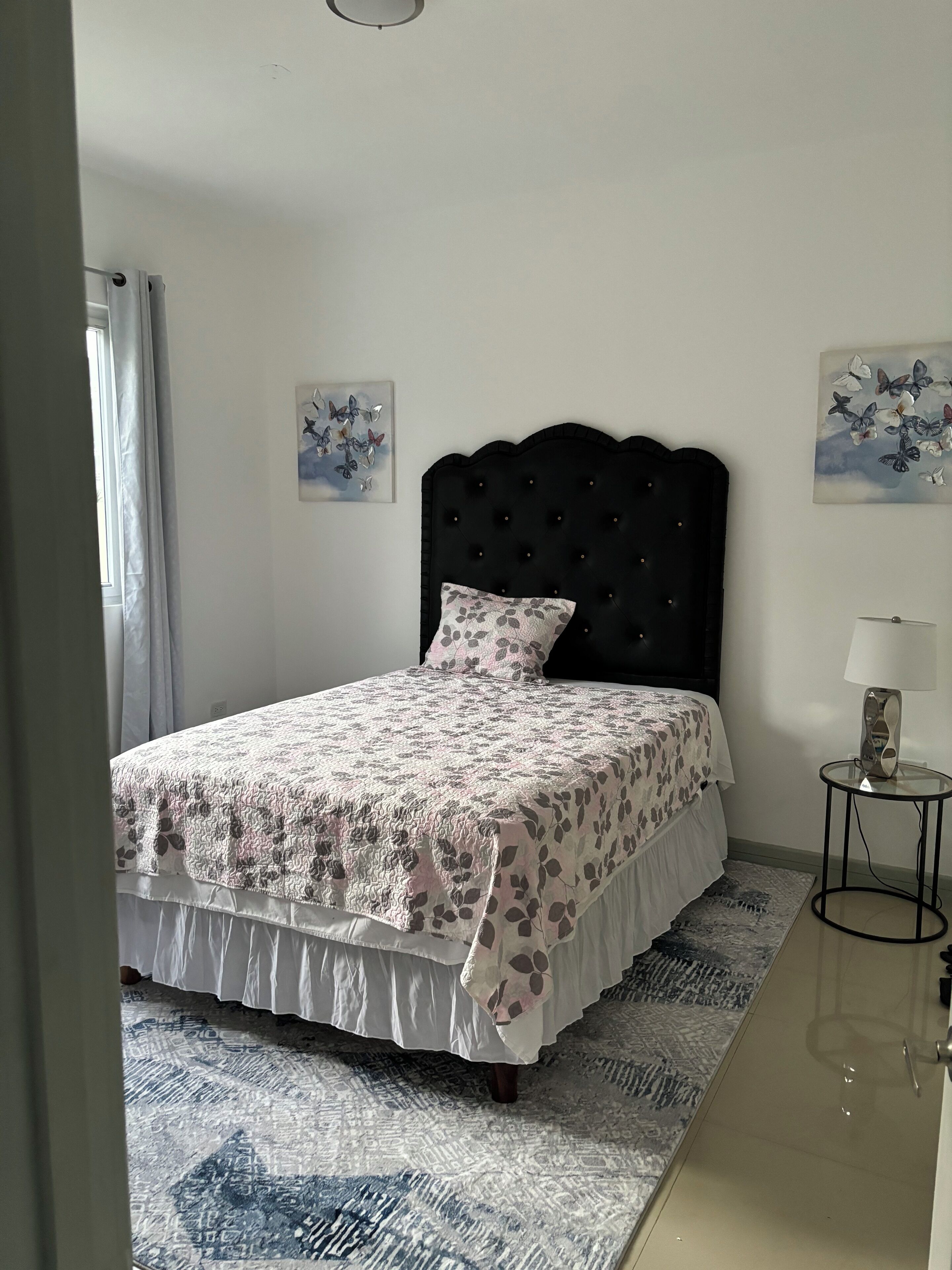 Un dormitorio con una cama, una mesita de noche, una lámpara y dos adornos de pared con forma de mariposa.