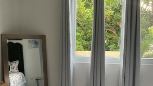 Een slaapkamer met een bed, een spiegel, een airconditioner en een raam met gordijnen.