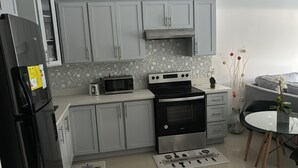 Een moderne keuken met grijze kastjes, een roestvrijstalen koelkast, een magnetron, een oven en een broodrooster. Er is een betegelde achterwand en een kleine eettafel met een placemat.