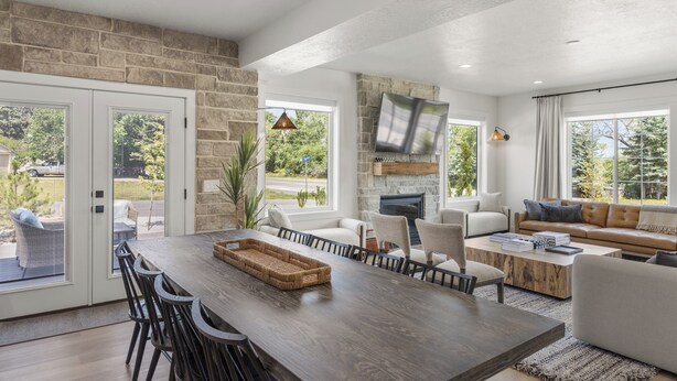 A spacious living area with a large wooden dining table, comfortable seating, a stone accent wall, and large windows offering a view of the outdoors.