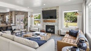 A modern living room with a stone fireplace, a flat-screen TV mounted above it, and a large window offering a view of the outdoors.