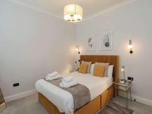 A neatly made bed with white linens and a brown throw blanket, a bedside table with a lamp, and two wall-mounted light fixtures. - The Salisbury 1 Bed Classic Apartment (Scarborough)