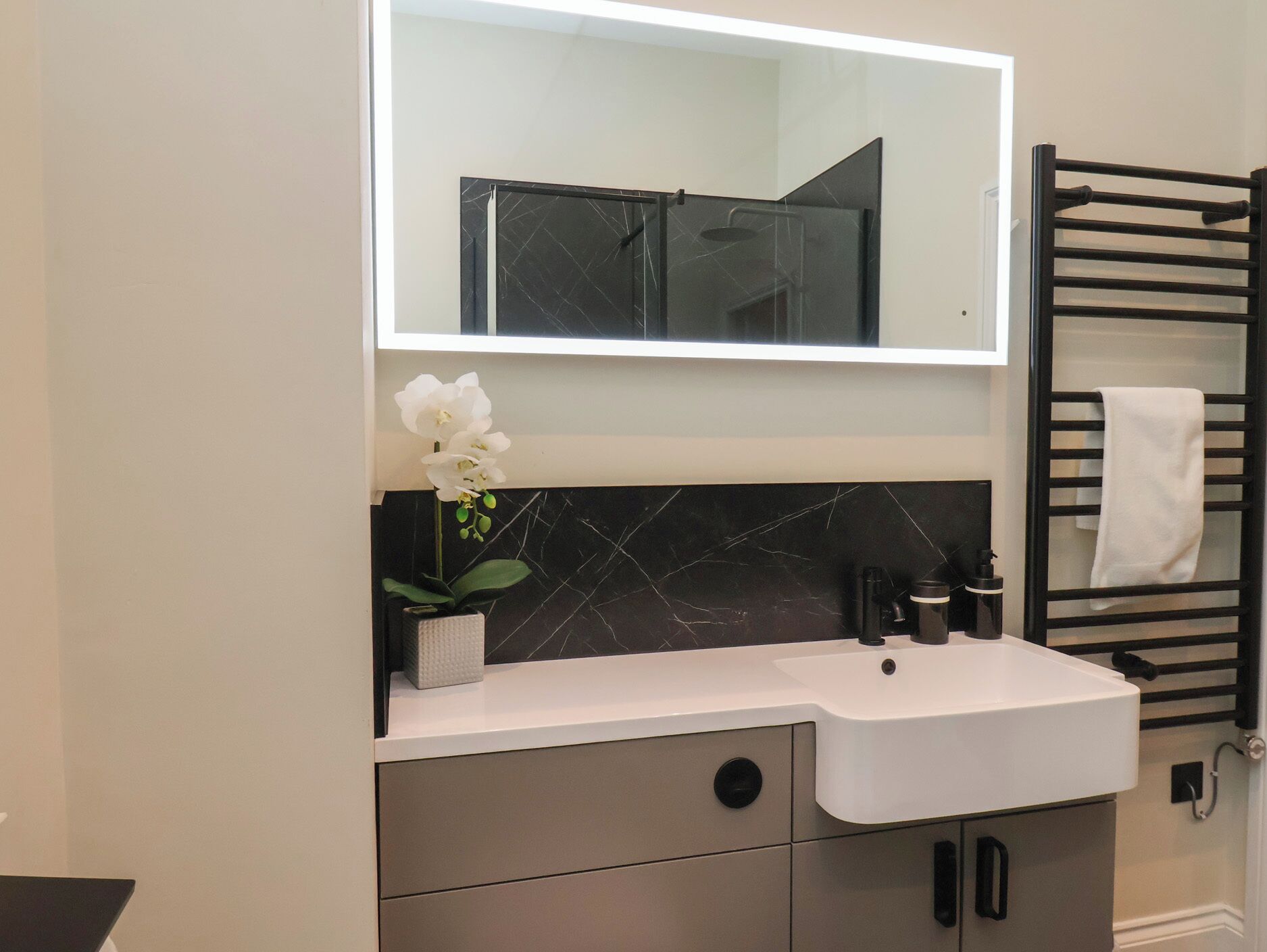 A modern bathroom with a white sink, black marble backsplash, a large mirror, and a towel rack.