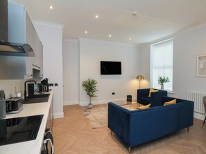 A modern living room with a blue sofa, a flat-screen TV, a coffee machine, and a potted plant. - The Salisbury 1 Bed Classic Apartment (Scarborough)