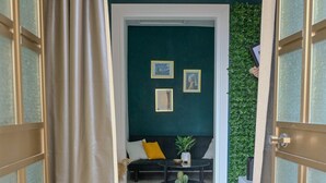 Une pièce avec un mur d’accent vert foncé, un canapé noir agrémenté d’un coussin jaune, une petite table ronde avec une plante, et un mur vert orné de feuillage.