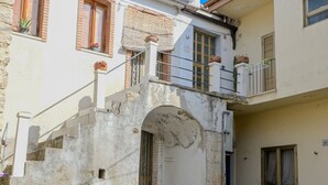Une cour avec un chemin pavé de pierres, une petite arche et un bâtiment doté d’un balcon et de plantes en pot.