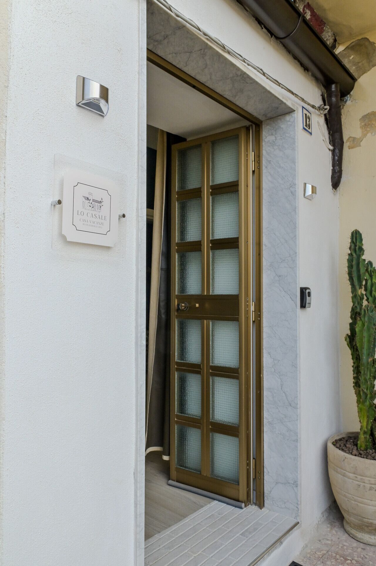 A hotel entrance with a glass door, a signboard, and a potted cactus.