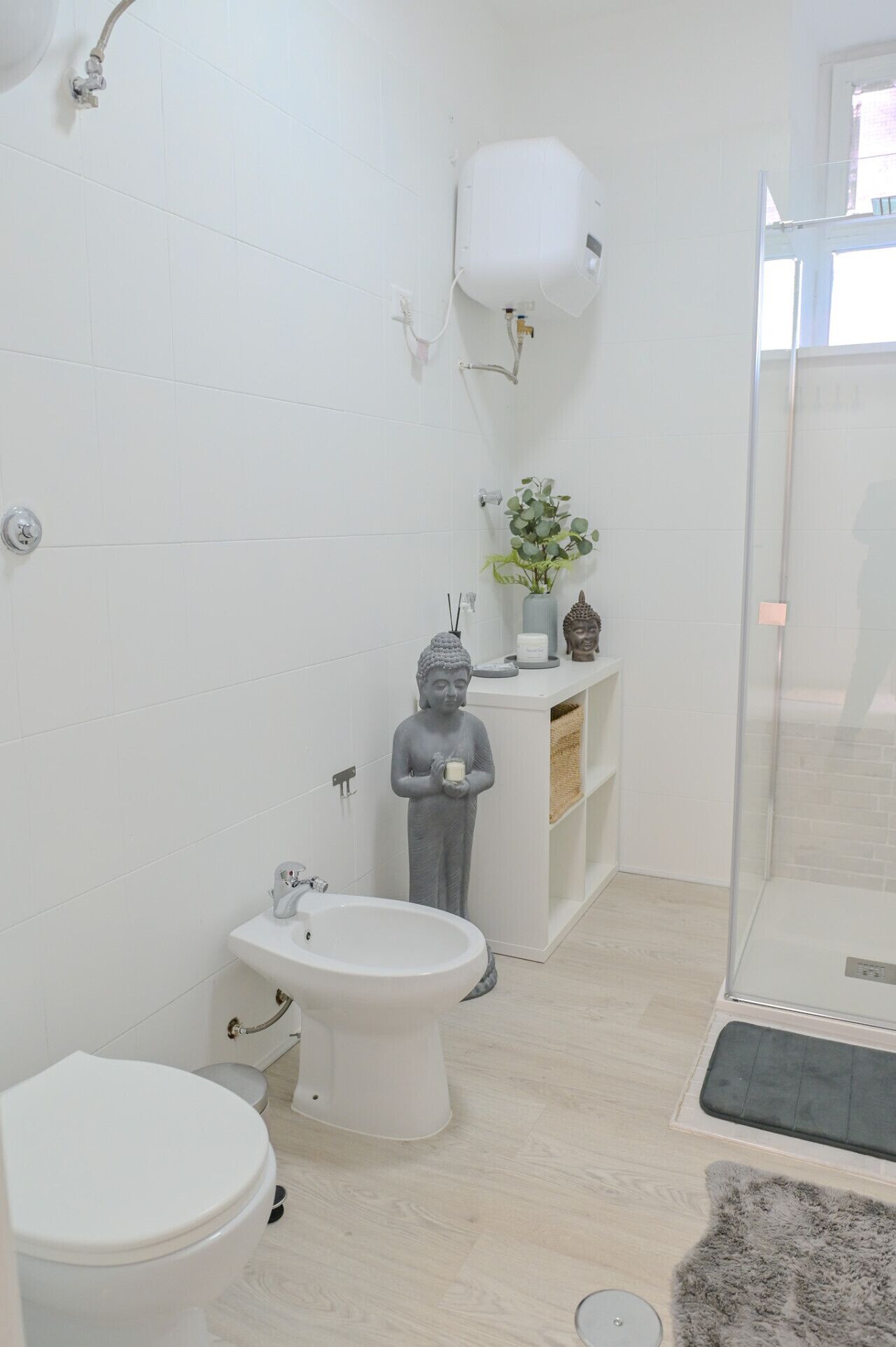 Un baño con azulejos blancos, un inodoro, un bidé, una ducha y una estatua.
