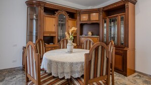 A dining area with a round table, six chairs, and a vase with flowers. There are wooden cabinets with glass doors and a marble floor. - Magnolia House - Appartamento 1 (Tor Lupara)